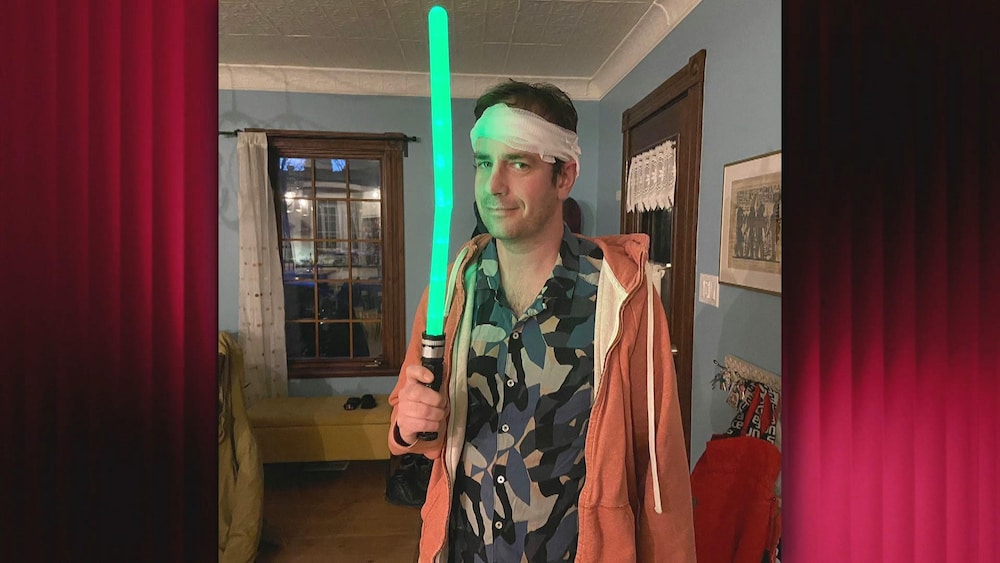 Robin-Joël Cool affiche un bandage sur la tête. Il tient dans une main une baguette lumineuse.