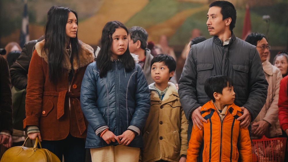Une famille debout, des valises dans les mains, au milieu d'une salle des fêtes.