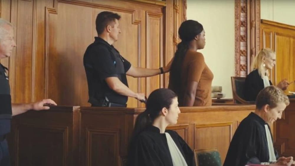 Un policier fait avancer une femme menottée dans une salle d'audience.