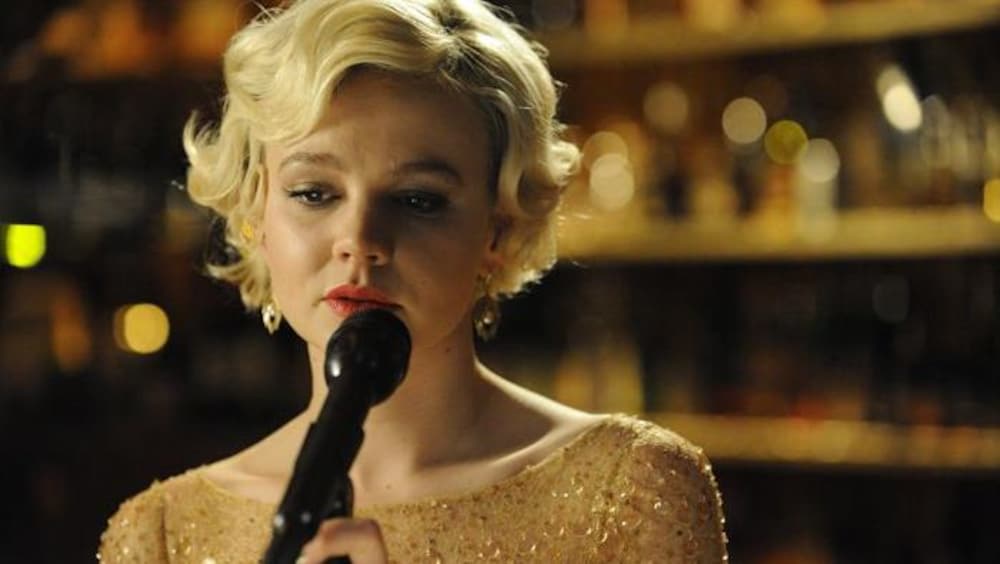 Alliance Vivafilm Une jeune femme blonde en robe à paillettes devant un micro.