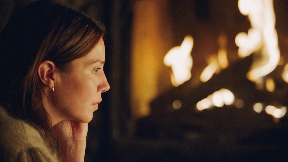 Une femme (Magalie Lépine-Blondeau) de profil devant un feu de cheminée.