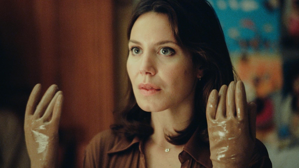 Une femme (Magalie Lépine-Blondeau), les mains gantées de plastique levées devant elle.