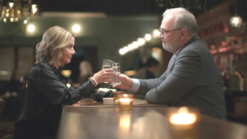 Une femme et un homme qui cognent leurs verres. Le couple se regarde dans les yeux.