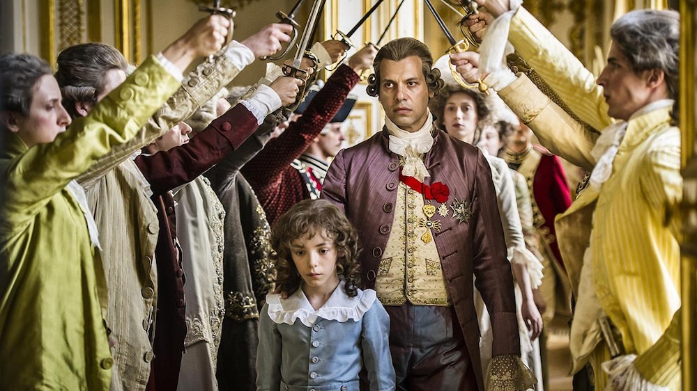 Jerome Prebois Le roi (joué par Laurent Laffitte) derrière un petit garçon passe sous une haie d'honneur de ses nobles.