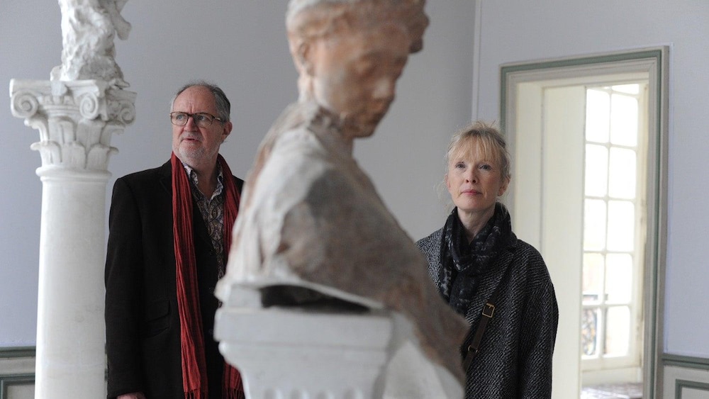 Un homme et une femme dans un musée, devant un buste en marbre.