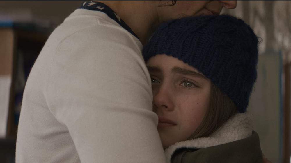 Une jeune fille portant un bonnet, les yeux pleins de larmes, collée contre une femme.