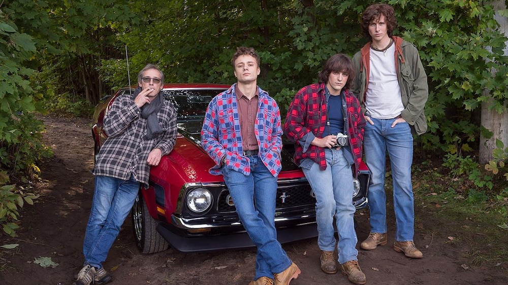 Le réalisateur Louis Bélanger et trois acteurs adossés sur une voiture rouge, sur un sentier.