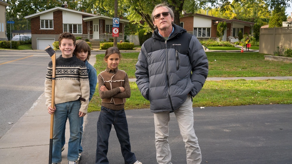 Le réalisateur Louis Bélanger à côté de trois enfants, dans une rue.