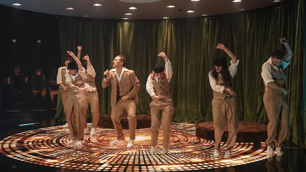 KOTV / Benoît Rousseau Pascal Morrissette, entouré de danseurs qui pointent vers le haut, créant une ambiance festive.