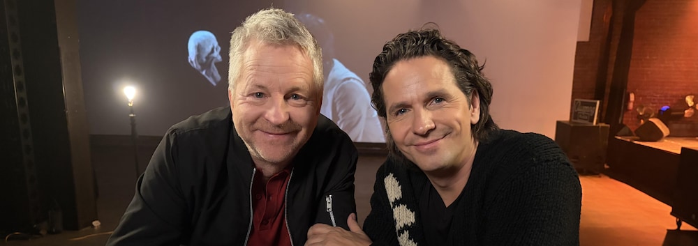 Andr&eacute; Robitaille et Guillaume C&ocirc;t&eacute; assis derri&egrave;re une table. Guillaume pose sa main sur le bras d'Andr&eacute;.