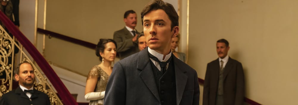 Lors d'une réception, Max Liebermann (Matthew Beard) tient un verre.