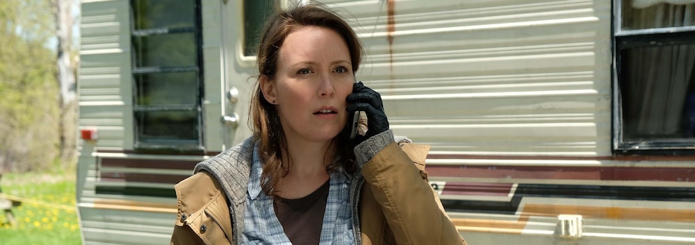 Constance Forest (Isabelle Blais) parle au téléphone à côté d'une roulotte de camping.