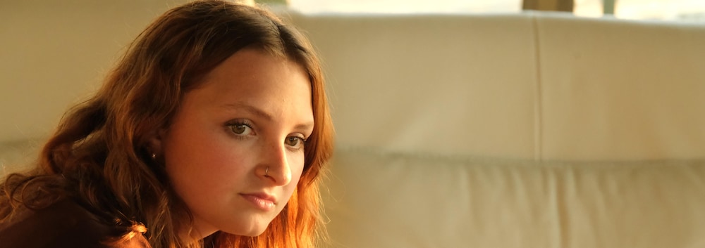 Une jeune femme penchée par en avant qui regarde quelque chose ou quelqu'un qu'on ne voit pas. Elle est assise sur un divan.