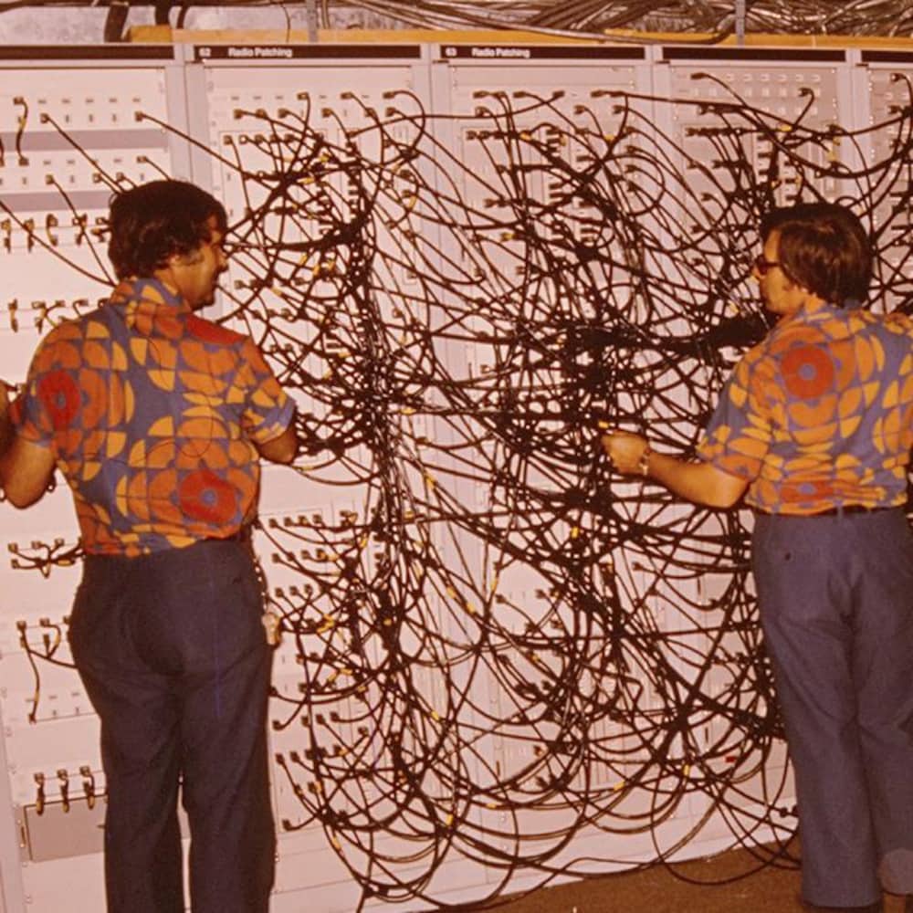 Trois techniciens de Radio-Canada pendant les Jeux olympiques d’été de 1976, devant un panneau de répartition pour le son.
