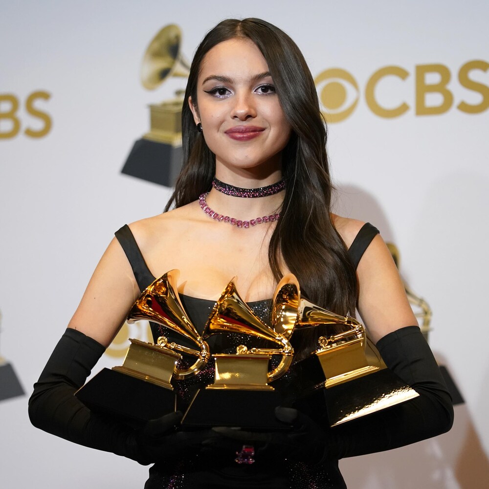 Olivia Rodrigo est debout avec trois prix Grammy dans ses mains.
