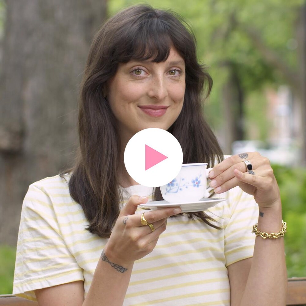 Sarah-Maude Beauchesne, assise sur un banc de parc, avec une tasse de thé à la main, regarde la caméra en souriant.