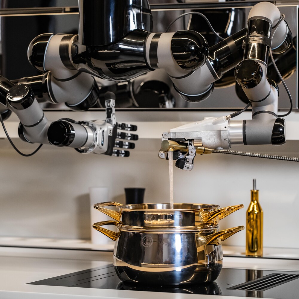 Un robot à deux bras est suspendu au-dessus d'une cuisinière. Une main robotique donne un coup de pouce et l'autre main verse de l'eau dans une marmite.