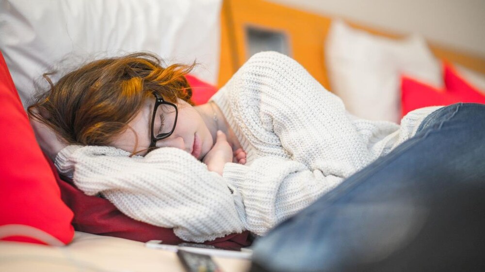 On voit une ado rousse à lunettes dormir dans un sofa