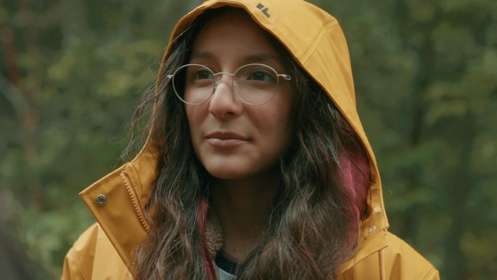 L'adolescente est dans la forêt et porte un imperméable. 