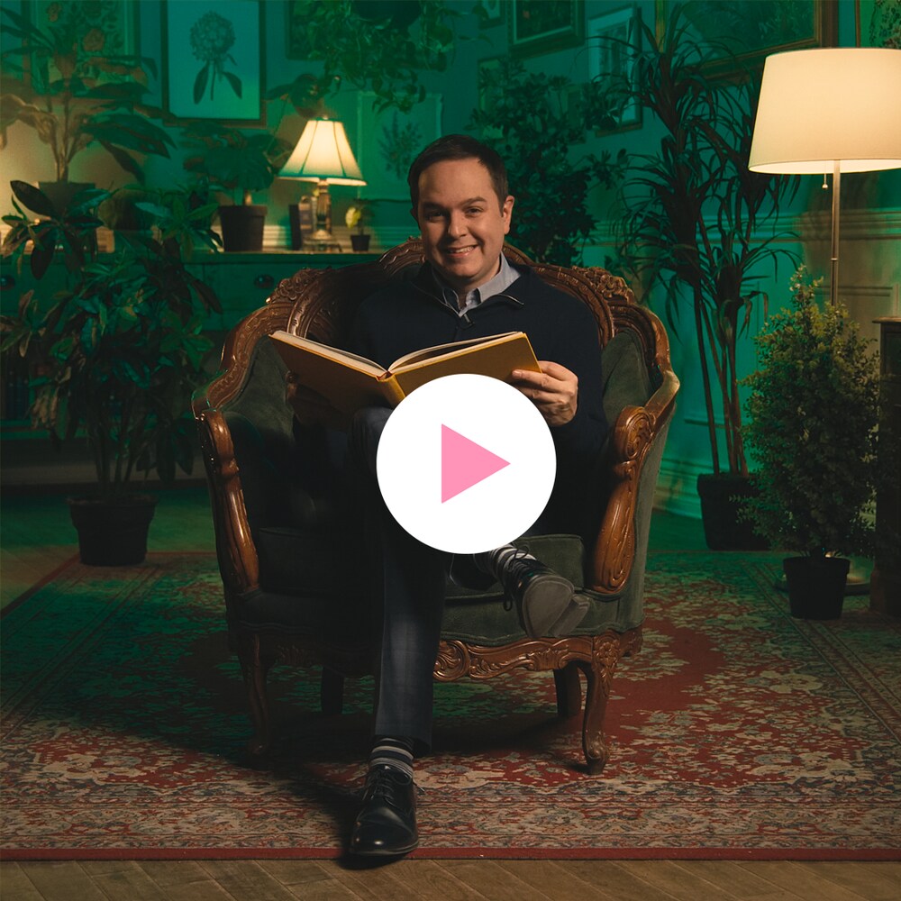 Gérald Filion est assis dans un fauteuil sur un tapis dans une pièce entourée de plantes et de tableaux botaniques encadrés.