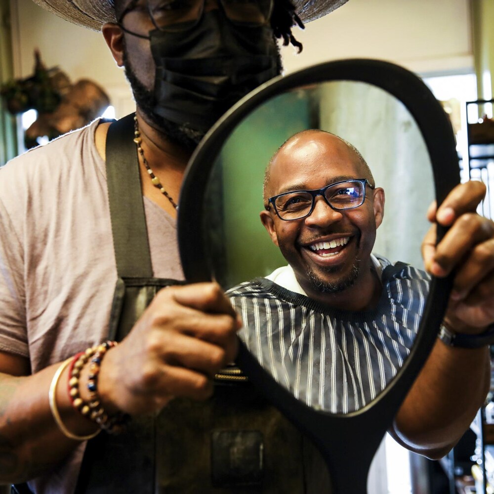 Un coiffeur tient un miroir devant un client qui sourit.