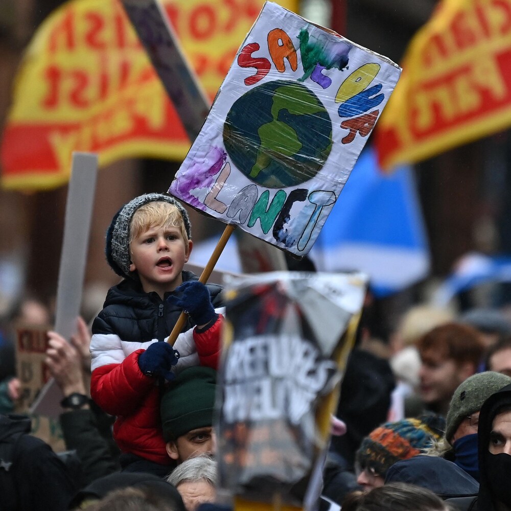 Un jeune tient une pancarte qui dit « Sauve notre planète » dans une foule de manifestants.