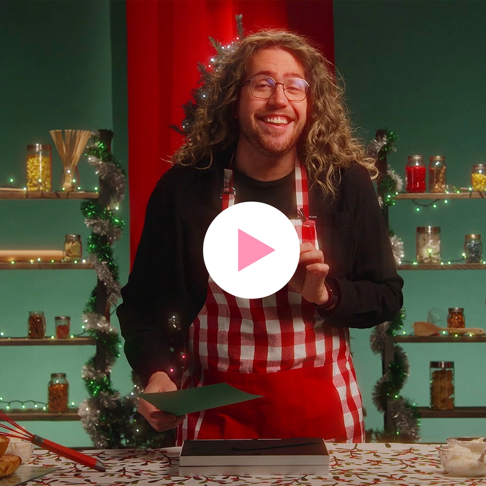 L'humoriste Mathieu Dufour se tient derrière une table sur laquelle sont déposés plusieurs gâteaux. Il porte un tablier de cuisine. Derrière lui se trouvent des étagères sur lesquelles des bocaux de nourriture sont placés. Les étagères sont décorées de lumières de Noël, ainsi que de guirlandes.