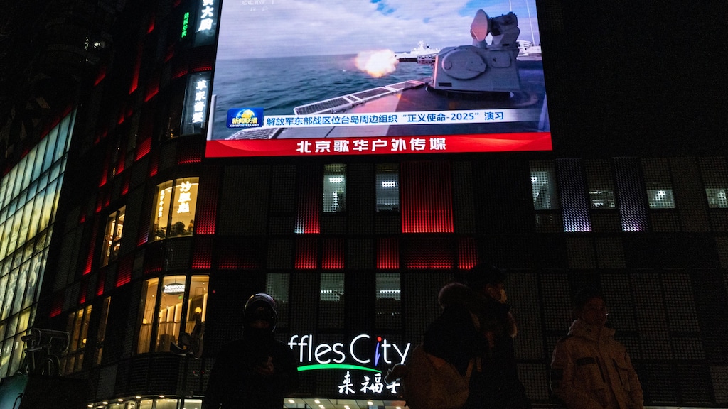 Un &eacute;cran montrant un navire militaire qui tire des munitions, dans la nuit d'une ville.