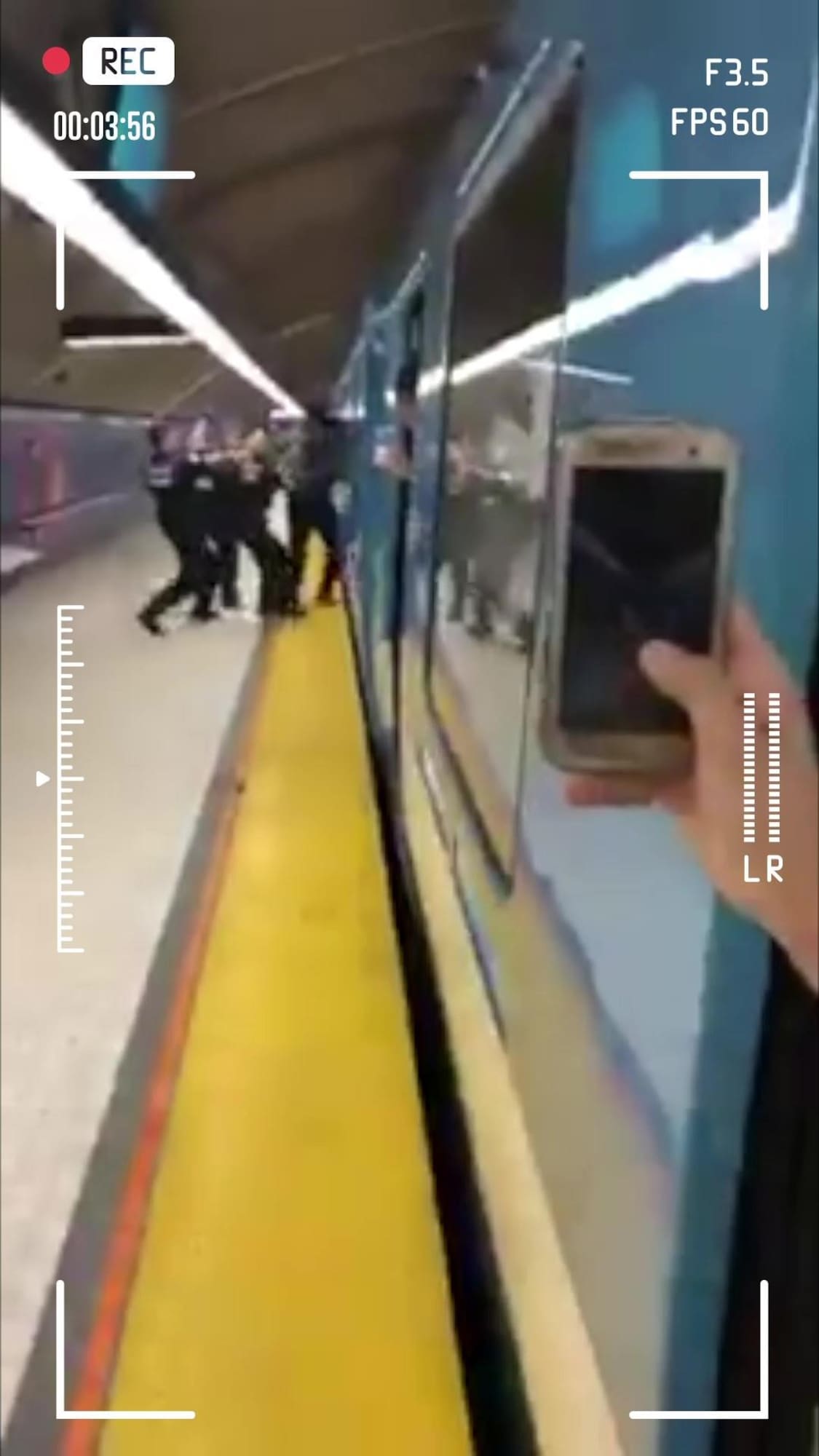 Une personne filme avec un téléphone intelligent des policiers qui tentent d'appréhender une personne et de la sortir d'un wagon de métro.