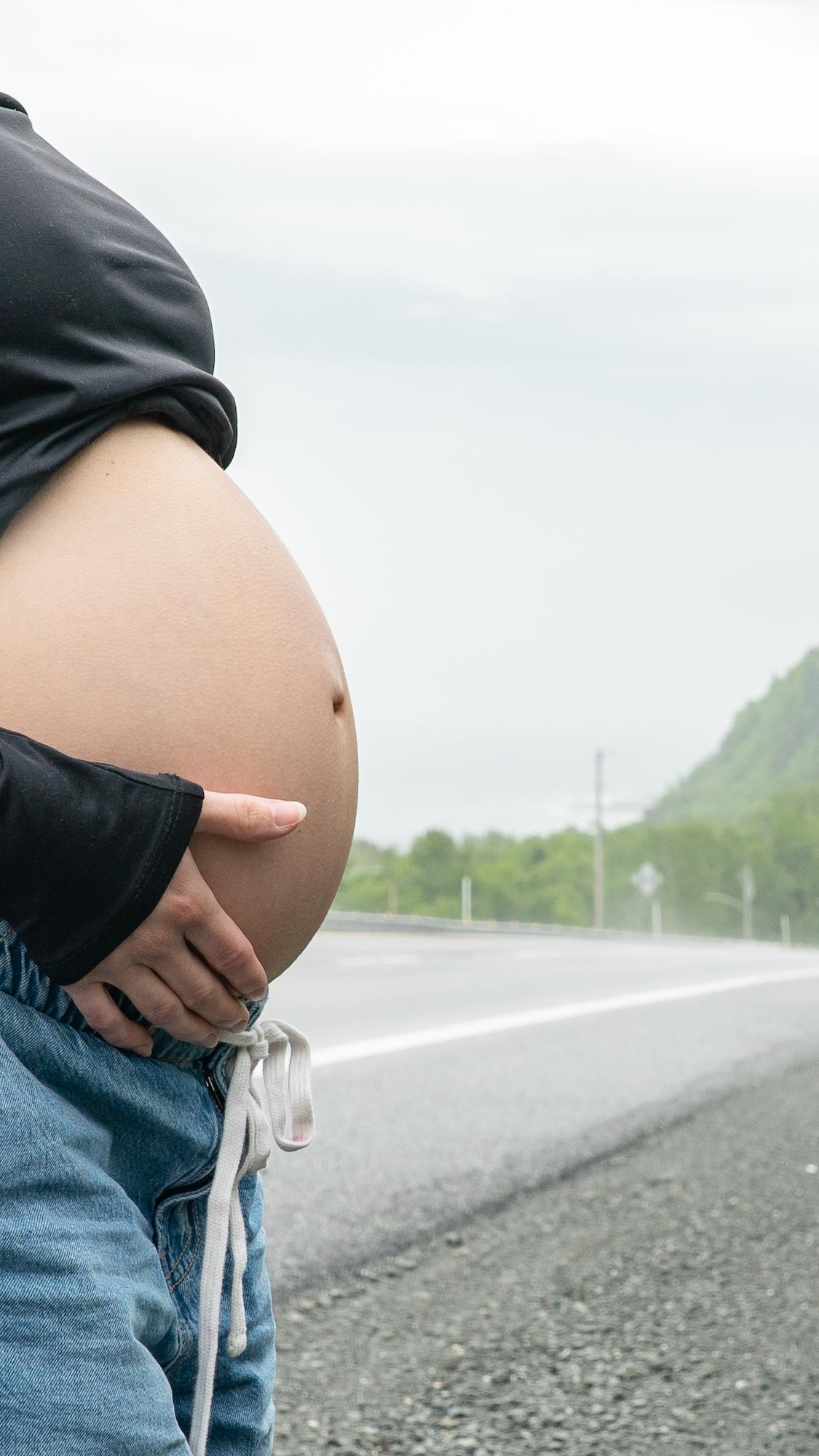 Une femme enceinte expose son ventre arrondi devant la route 132.