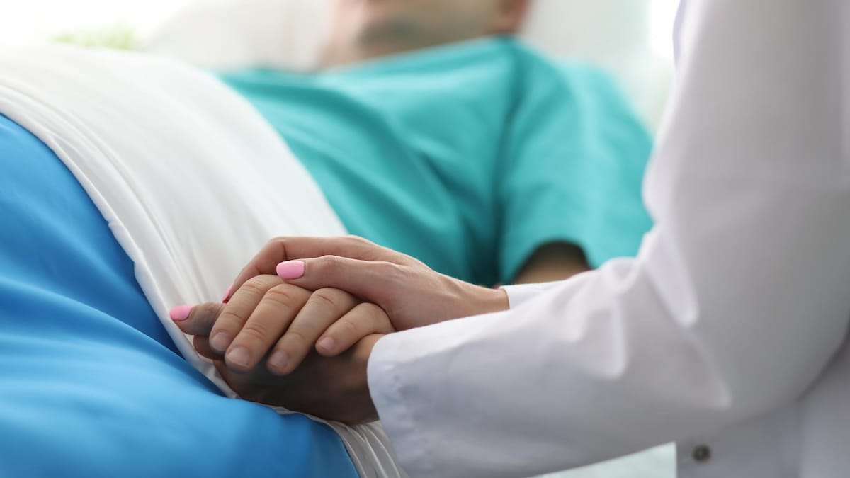 Une médecin tient la main d'un patient dans un lit.