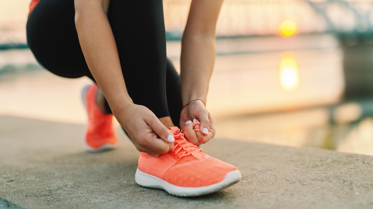 Au soleil couchant, une femme noue les lacets de son soulier de course.