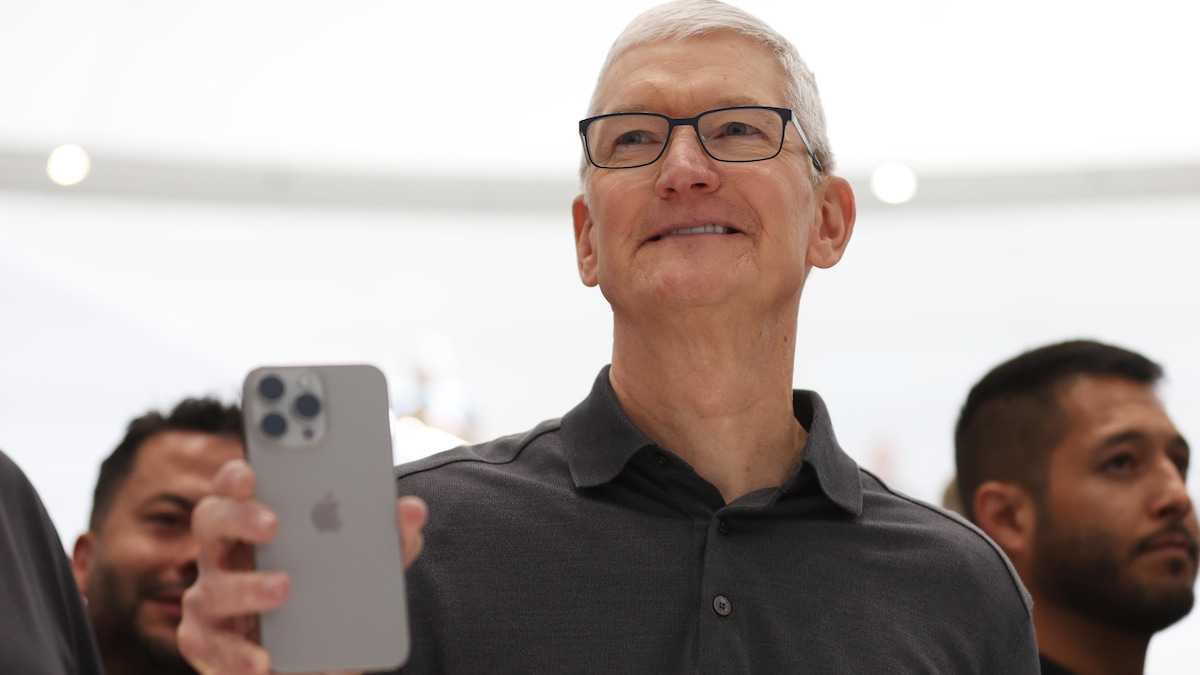 Tim Cook, souriant, tenant un iPhone dans la main, dans un Apple Store. 