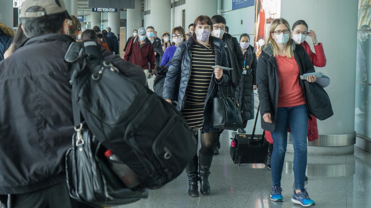 Des passagers portant un masque font la file dans un aéroport.