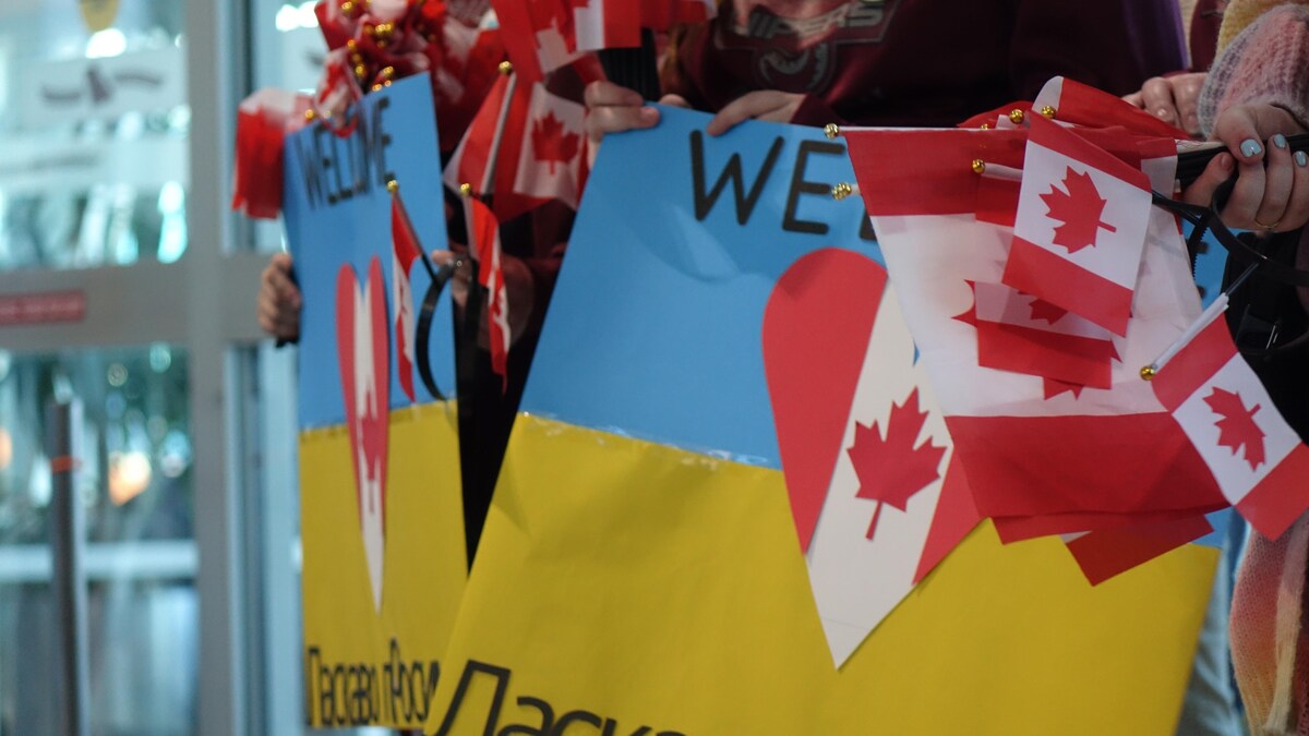 Une foule dans un aéroport accueille des réfugiés ukrainiens. Ils ont des drapeaux canadiens et ukrainiens dans les mains. 
