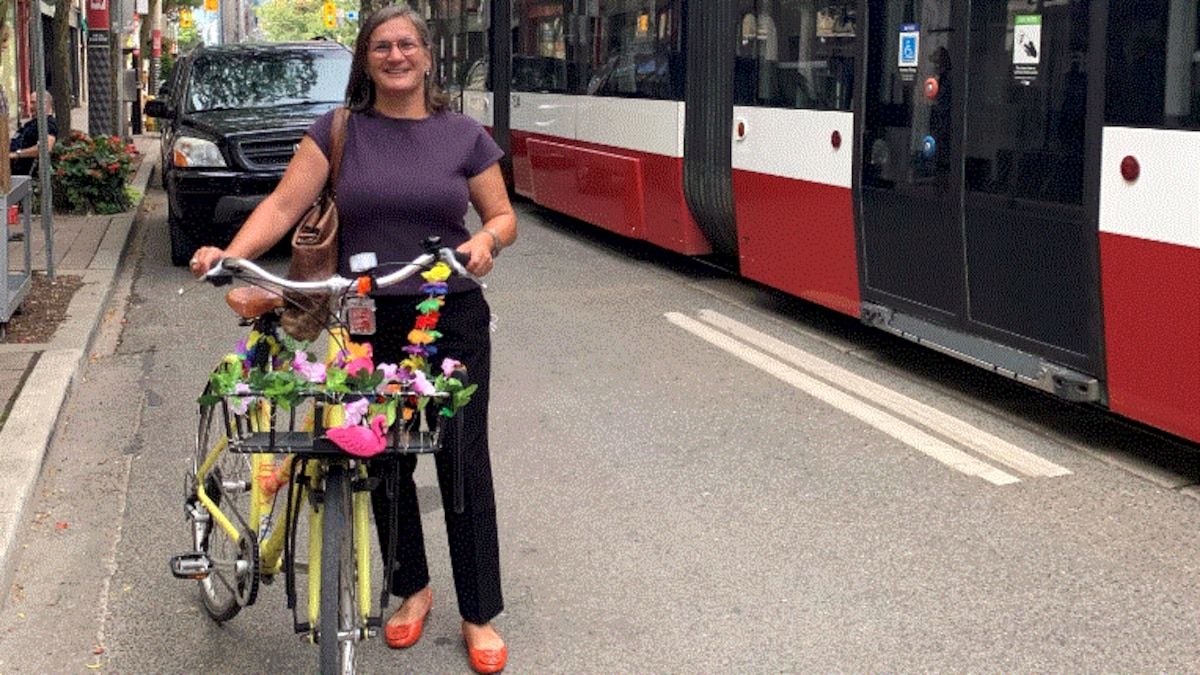 Alison Stewart debout devant un véhicule noir tient un vélo sur la chaussée à proximité d'un tramway.