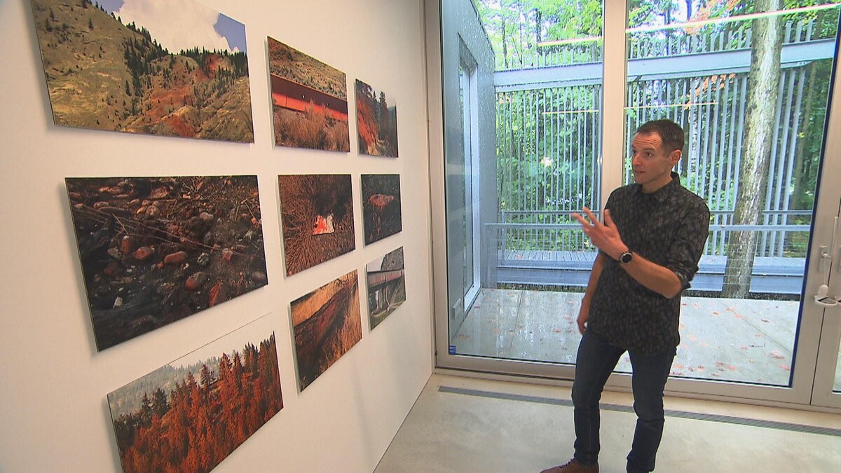 Un homme montrant des photos de forêts brulées accrochées sur un mur.