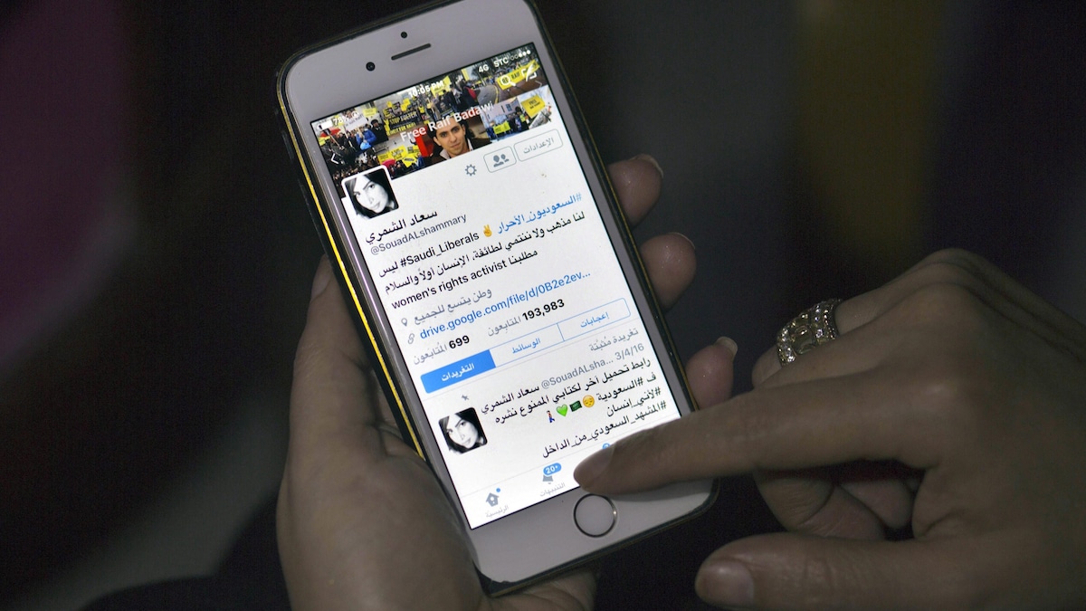 Une personne a la main sur l'écran d'un téléphone et regarde le compte de l'activiste féministe Souad al-Shammary.