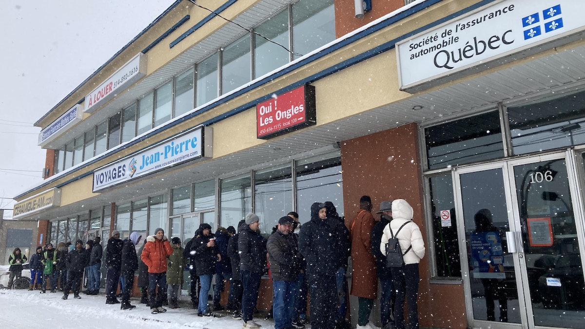 Une cinquantaine de personnes attendent dans la neige devant une succursale de la SAAQ. 