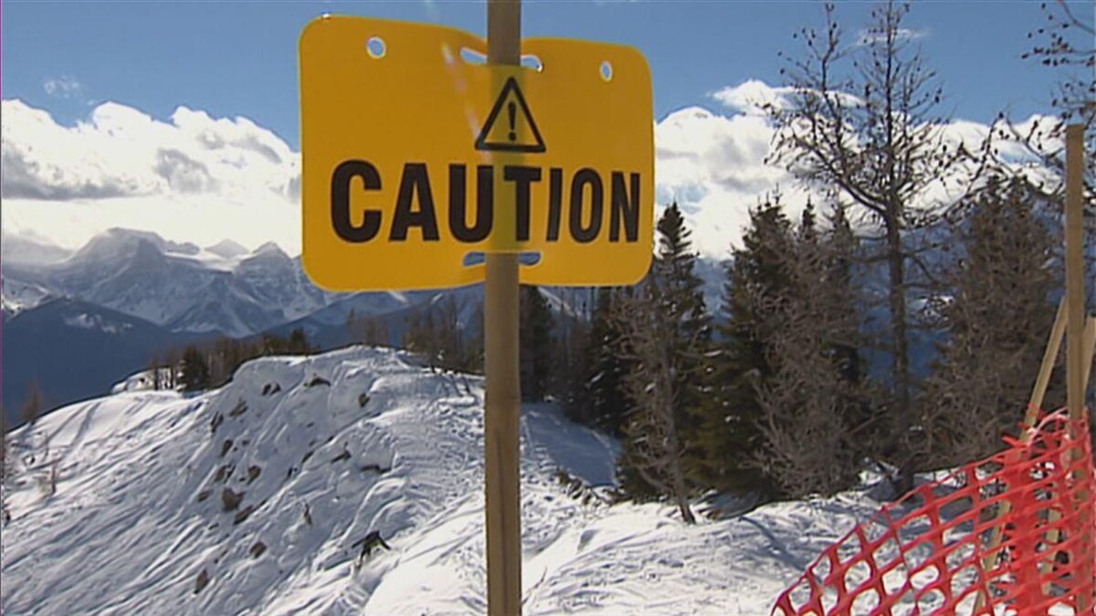 Une affiche jaune indiquant « ATTENTION » au sommet d'une montagne enneigée.