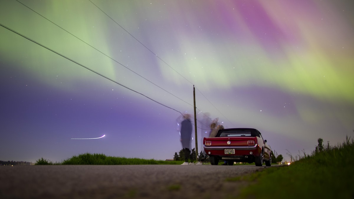 Des gens sont debout près de leur voiture sous un ciel drapé d'aurores boréales.