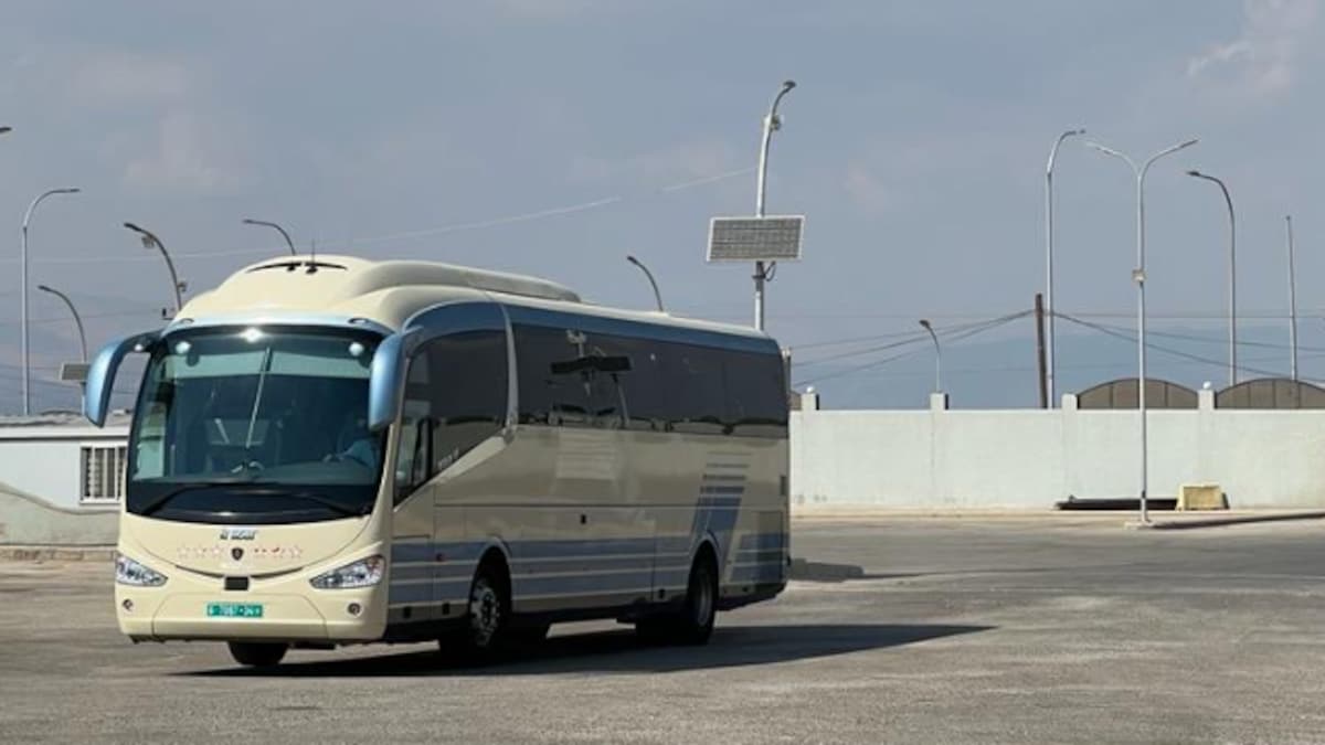 Un autobus franchit un poste-frontière entouré de barbelés et de murets de béton.