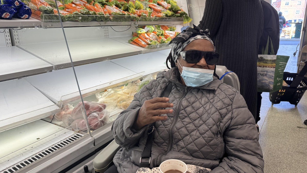 Gloria, assise dans son fauteuil motorisé, devant les étagères de la banque alimentaire.