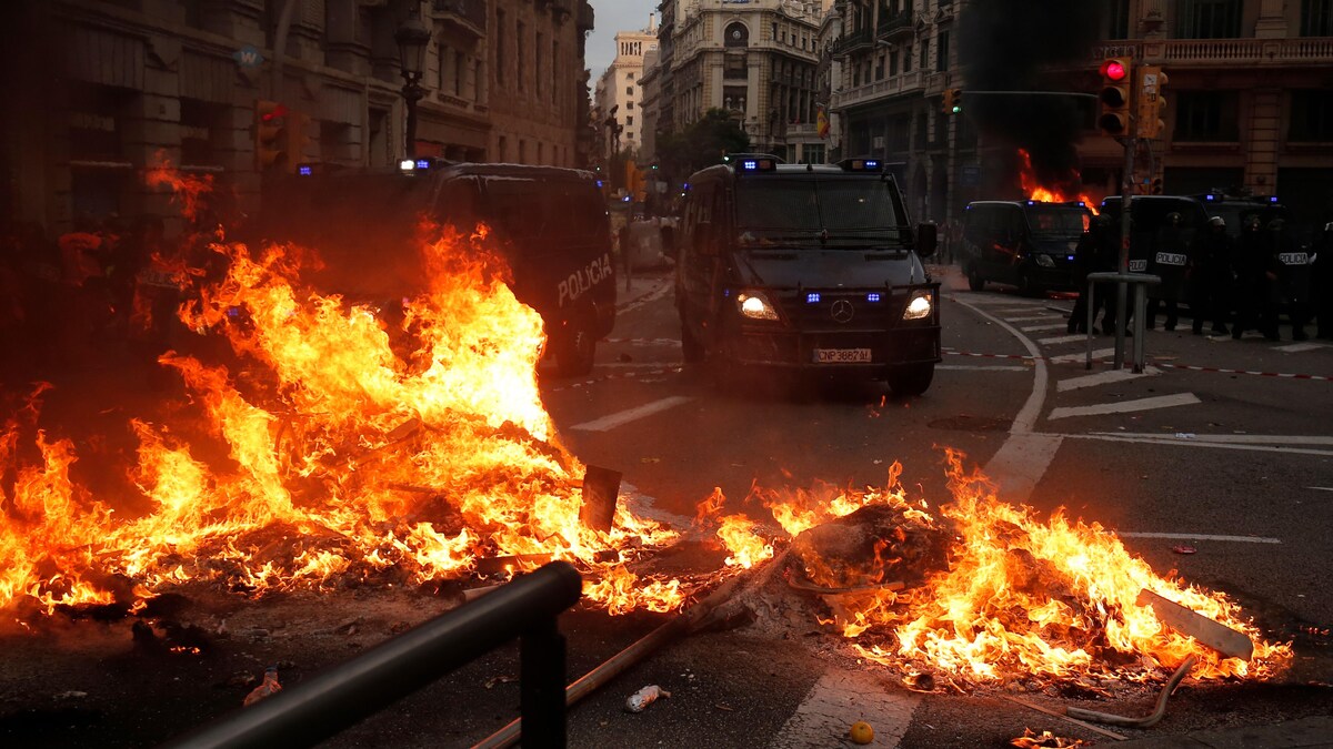 Des objets en feu au milieu d'une rue barrent le chemin aux camions de la police de Barcelone.