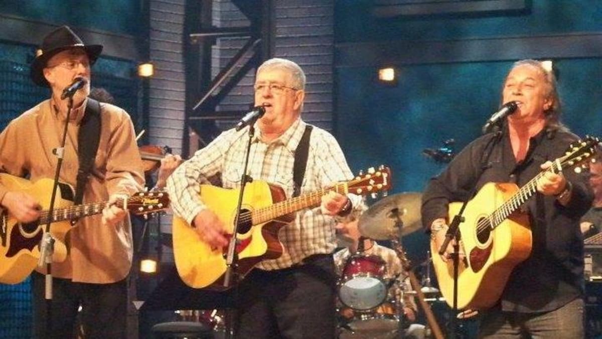 Bernard Harvie, Jerry Cormier et Paul Daraîche chantent sur la scène en jouant de la guitare.