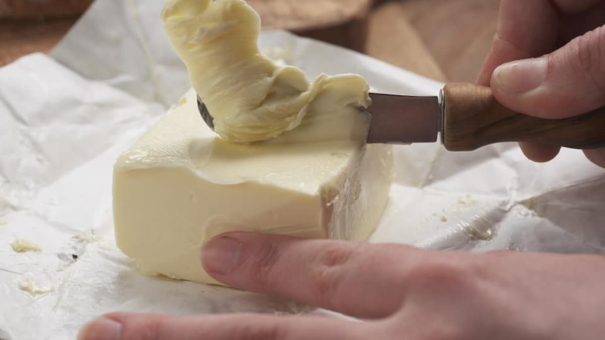 Gros plan sur des mains qui tiennent une brique de beurre et tartinent à l'aide d'un couteau à beurre. 

