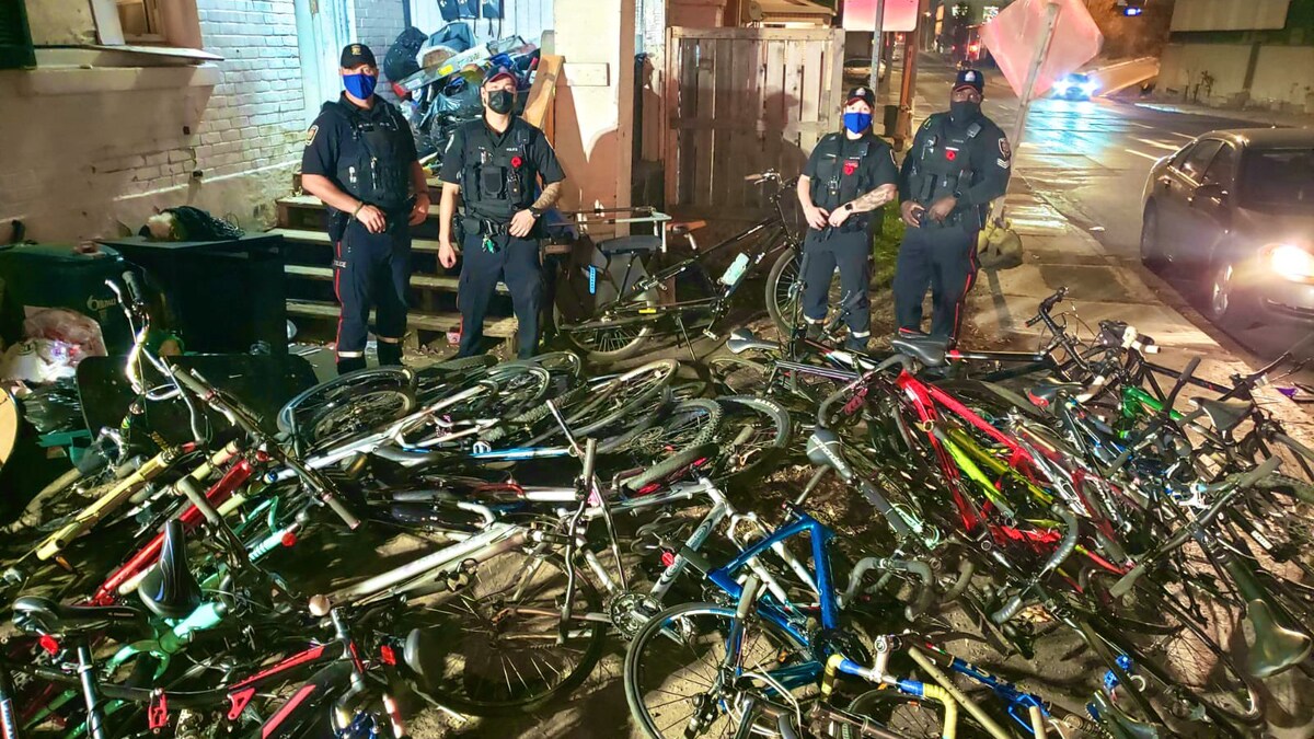 Une quarantaine de vélos sont empilés les uns sur les autres avec quatre policier derrière, installés pour une photo.