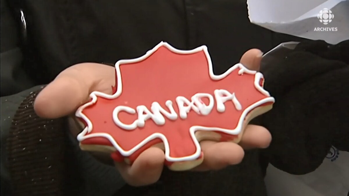 Biscuit en forme de feuille d'érable avec le mot Canada écrit en glaçage dans la main d'une jeune femme.