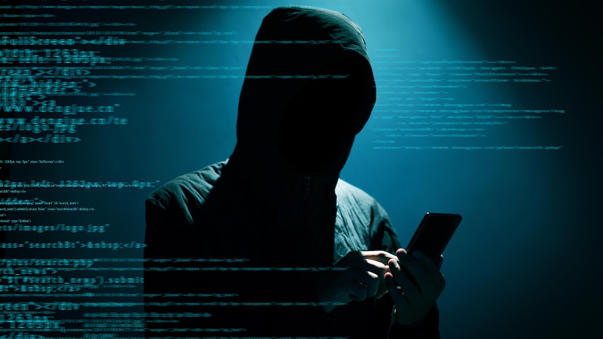 Une silhouette tenant un téléphone avec des codes informatiques.