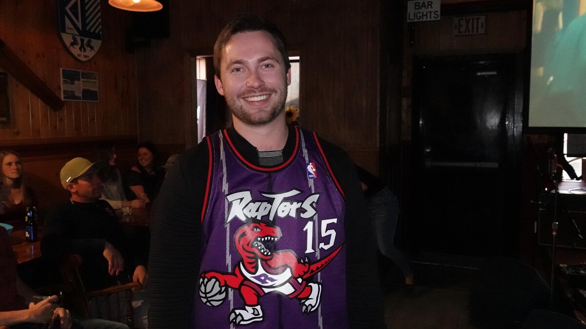 Un homme souriant vêtu des couleurs des Raptors de la NBA. 